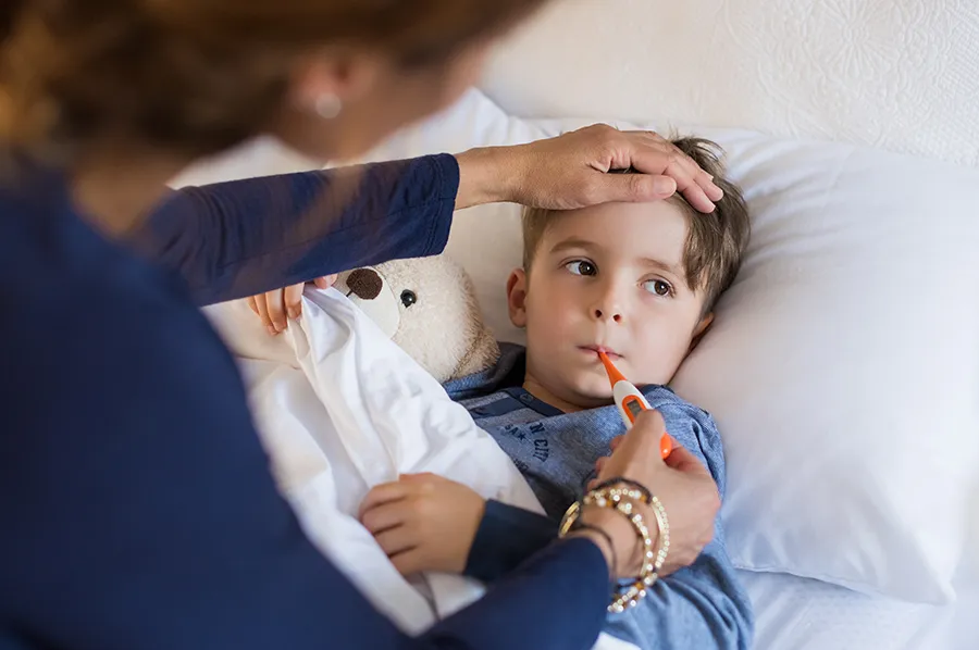 Parent caring for a sick child in bed while checking for fever, illustrating common pediatric illness symptoms
